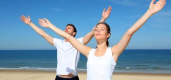 Couple meditating at the beach with arms up